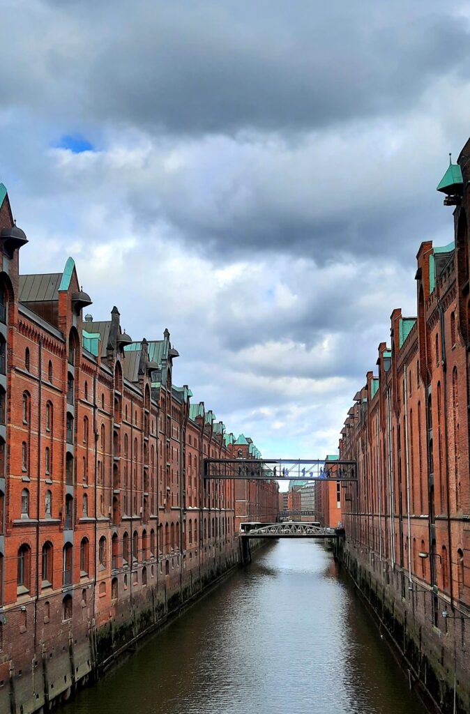 Historic red-brick warehouses lining a canal in Hamburg’s Speicherstadt district, with bridges connecting the buildings beneath a cloudy sky