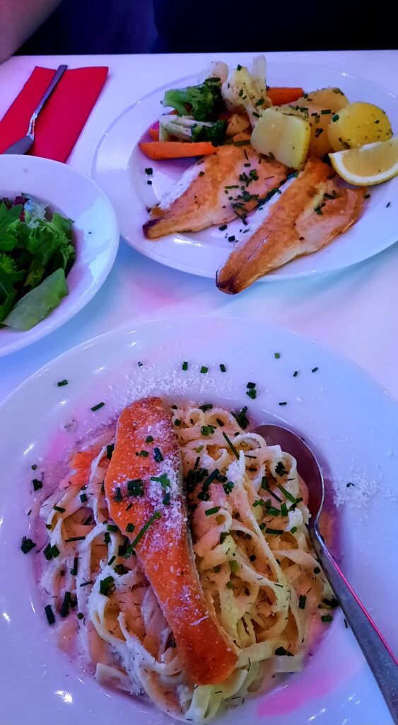 Fish fillets with potatoes and vegetables, alongside a seafood pasta dish, served at Störtebeker in Hamburg.