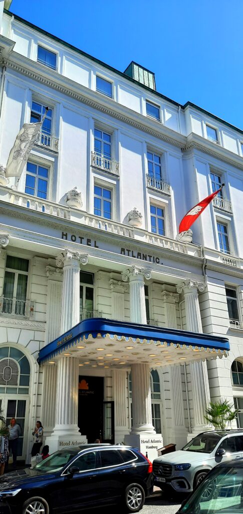 Exterior of Hotel Atlantic in Hamburg, showing its white historic façade, entrance canopy and red flag.