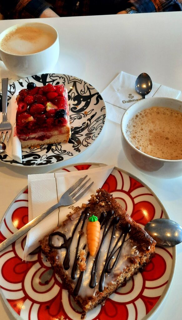 Two cups of coffee with slices of berry cake and carrot cake on colourful plates at a bakery near Nymphenburg Palace in Munich.