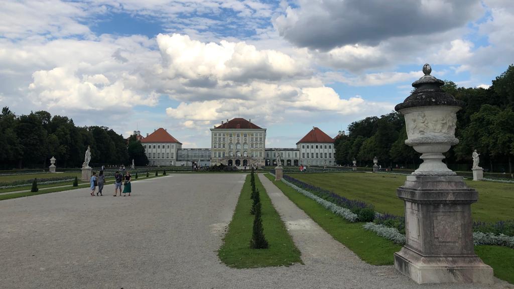 View of Nymphenburg Palace in Munich, with landscaped gardens, walking paths and a stone urn in the foreground.