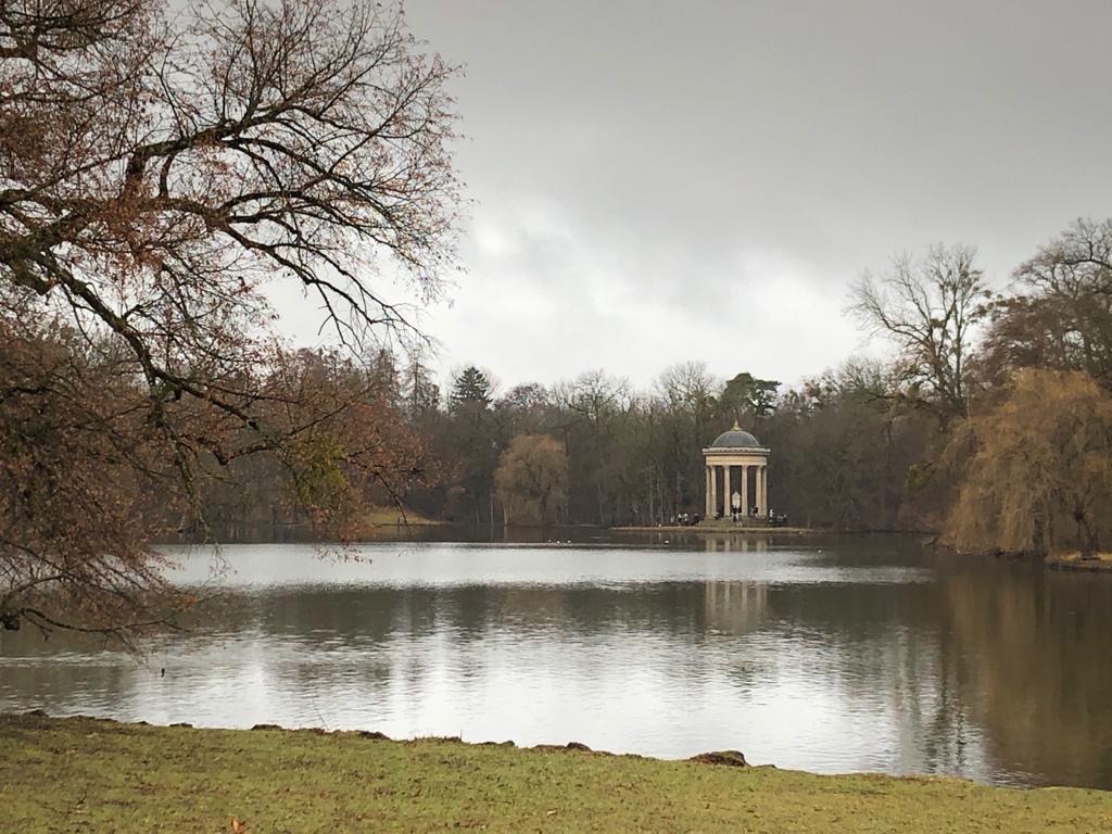 Temple of Apollo across the lake in Nymphenburg Palace Park, Munich, surrounded by trees and reflected in the water.
