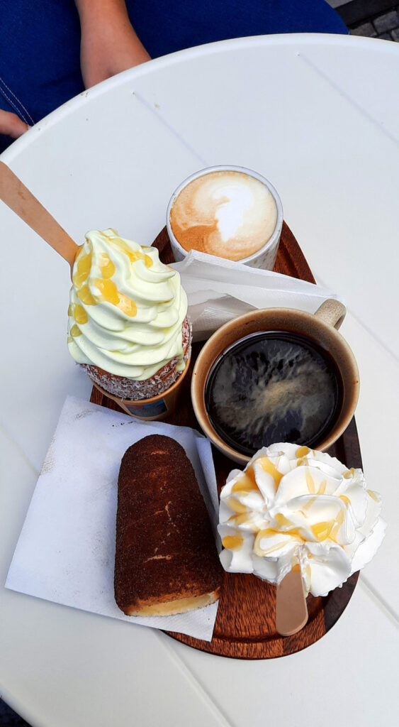Chimney cakes with ice cream and toppings, a classic chimney cake, and two coffees served on a wooden tray in Prague.