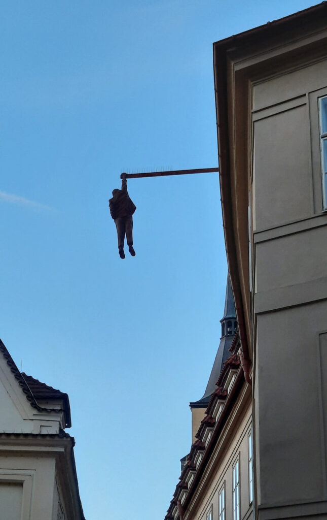 Hanging Man sculpture by David Černý, depicting a figure suspended from a beam above a street in Prague.