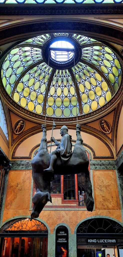 David Černý’s sculpture of a man riding an upside-down horse beneath an ornate glass dome in Lucerna Passage, Prague.