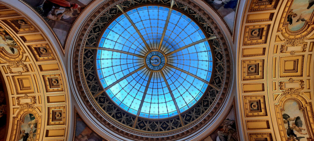 Ornate ceiling and circular blue glass dome inside the National Museum in Prague, surrounded by decorative architectural details.