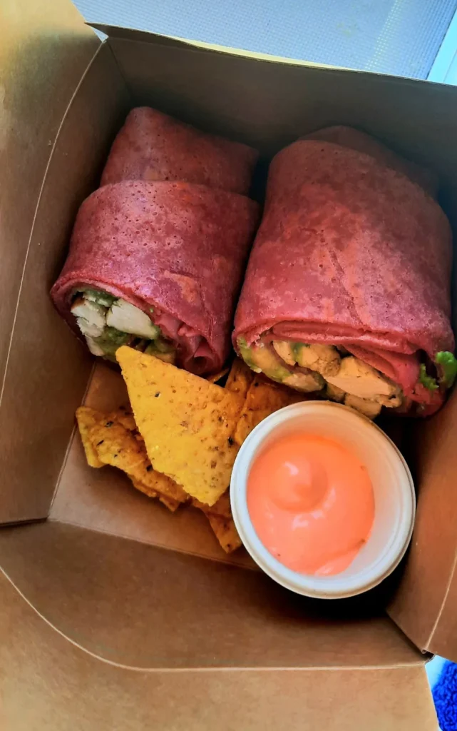 Two tofu and avocado wraps with tortilla chips and dipping sauce in a takeaway box