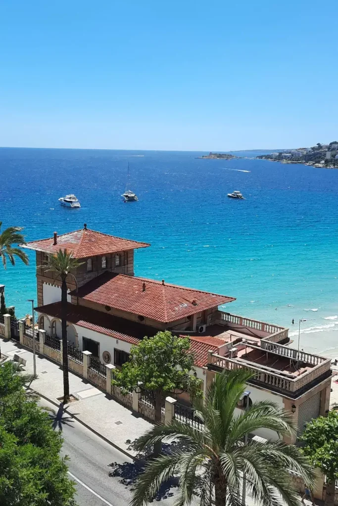 Turquoise Mediterranean Sea, boats and palm trees overlooking Cala Major beach in Mallorca