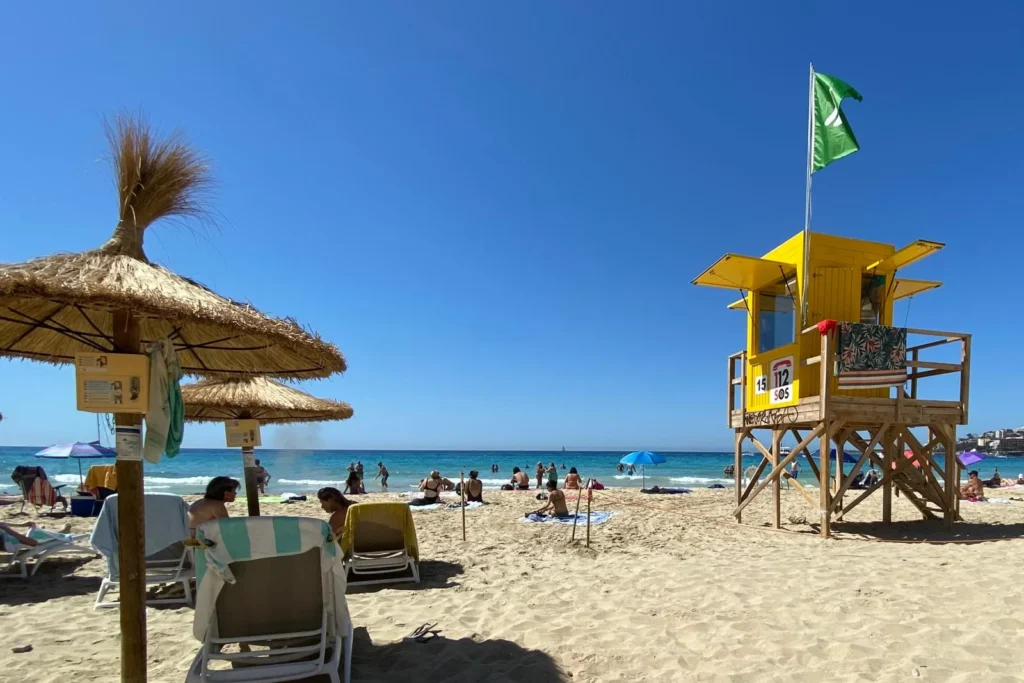 Sun loungers beneath straw umbrellas with small attached safes on Cala Major beach in Mallorca