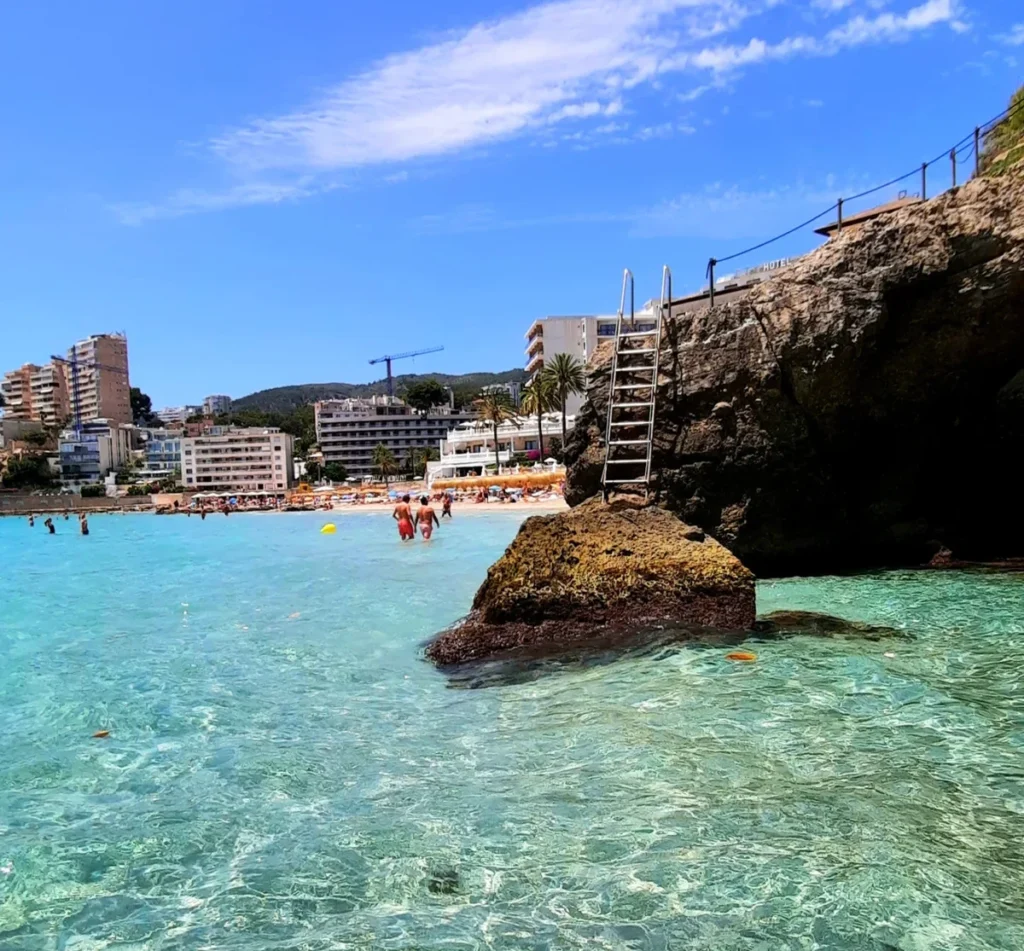Clear turquoise water and rocky shoreline at Cala Major beach in Mallorca, with a swimming ladder leading into the sea.