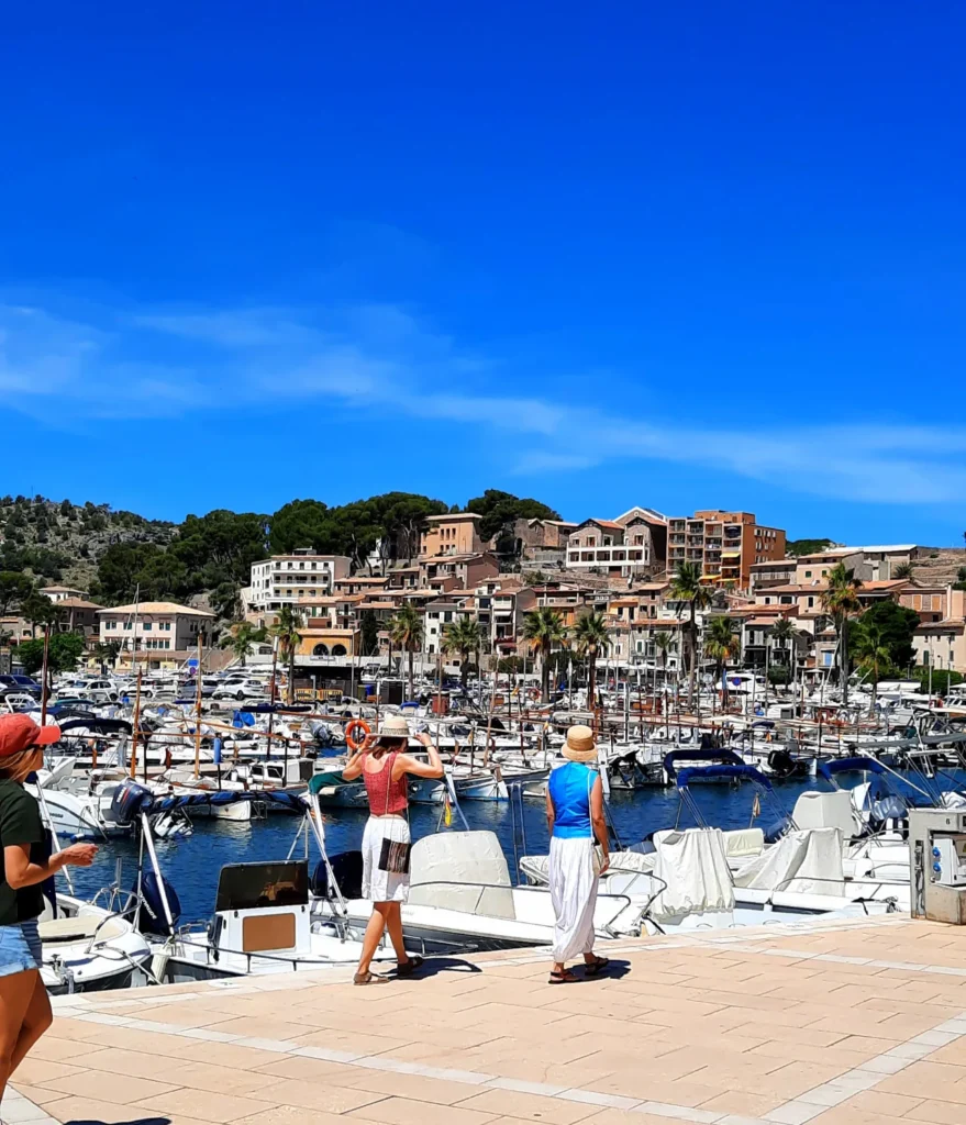 Boats moored in Port de Sóller harbour in Mallorca, with waterfront buildings and green hills in the background