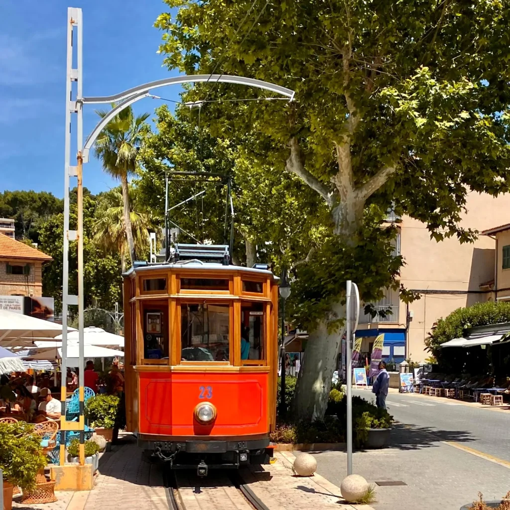 Historic red and wooden tram number 23 in Port de Sóller, Mallorca, surrounded by trees and cafés